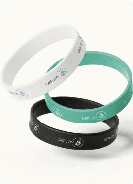Three silicone wristbands stacked: one white, one teal, and one black, each with the word "DEPLOY" and a small circular logo featuring a symbolic design.