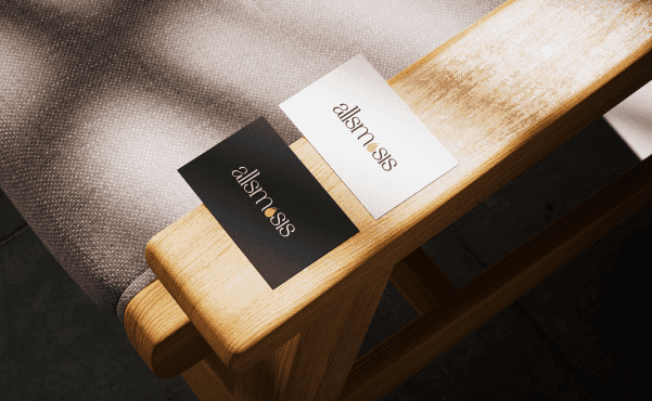Two business cards, black and white, with "allsmosis" text in gold highlight are placed on a wooden chair armrest, next to textured fabric.
